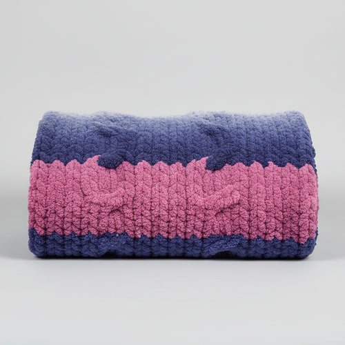 photo of blue/pink gradient cable pattern blanket folded on a gray backdrop