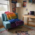A photo of a textured pattern rainbow blanket on a teal chair in a bedroom