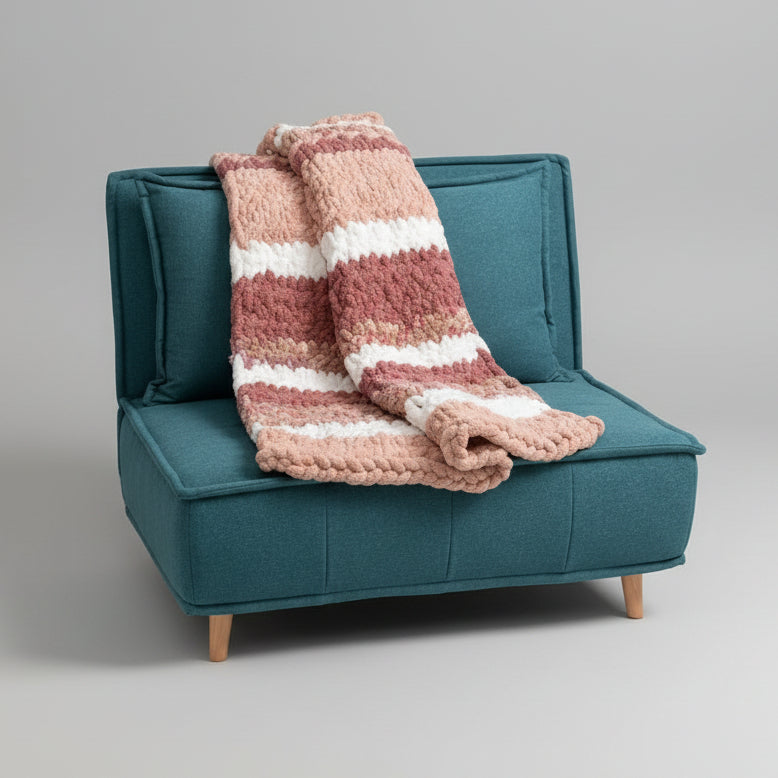 A photo of a teal chair with a small throw blanket colored in a rose and neutral palette.