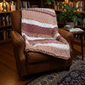A photo of a beige and rose colored chair throw blanket on a brown leather chair. 