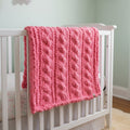 Photo of Pink knit baby blanket draped over crib rail