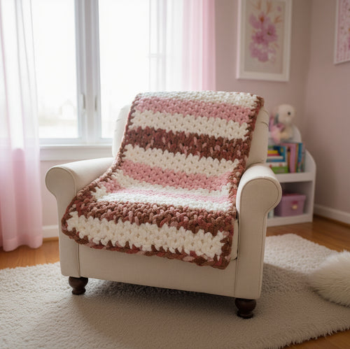 A photo of a pink, cream and multi-brown toddler blanket draped on a cream chair