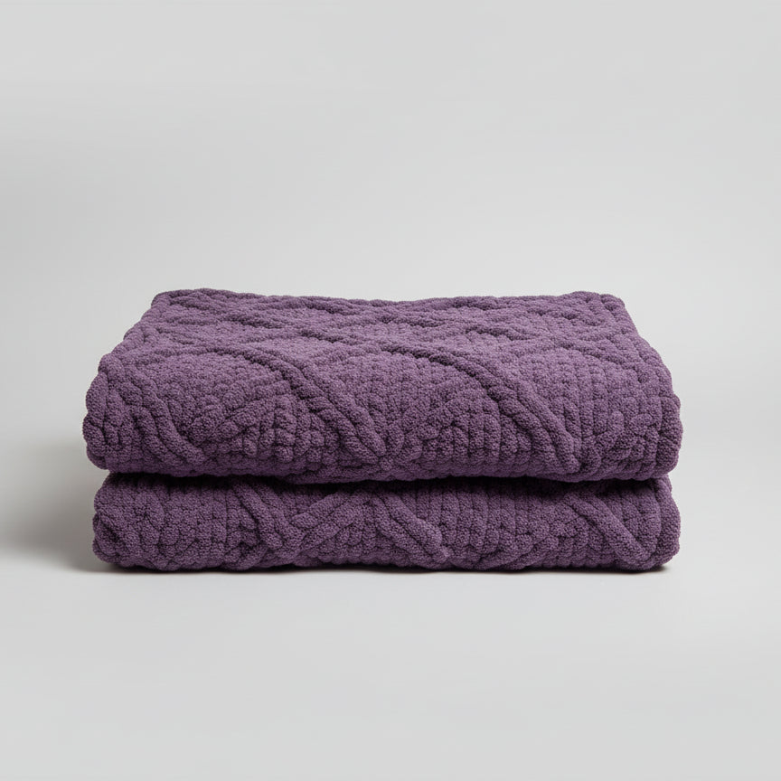 Purple knitted blanket draped over a teal chair next to a wooden nightstand with a lamp.