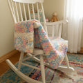 A photo of a baby blanket hanging over a rocking chair arm.